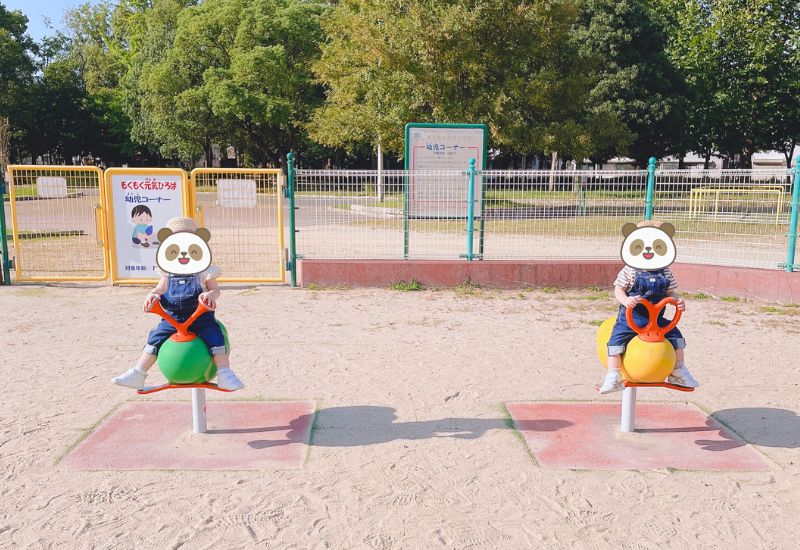 柵のある公園の遊具で遊ぶ双子の様子